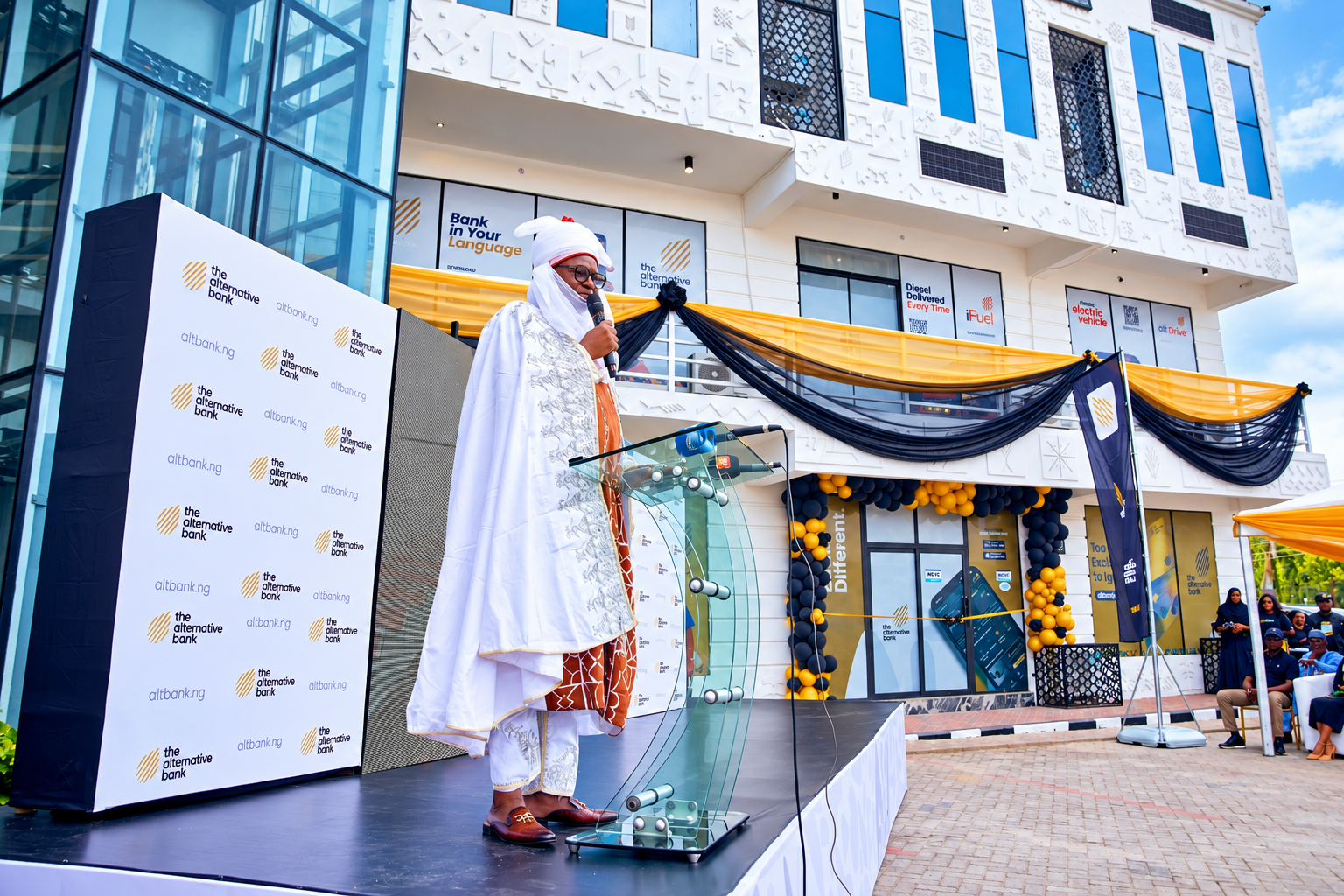 The Alternative Bank Gwarinpa branch opening ceremony in Abuja, with a traditional ruler speaking at a podium outside the bank.