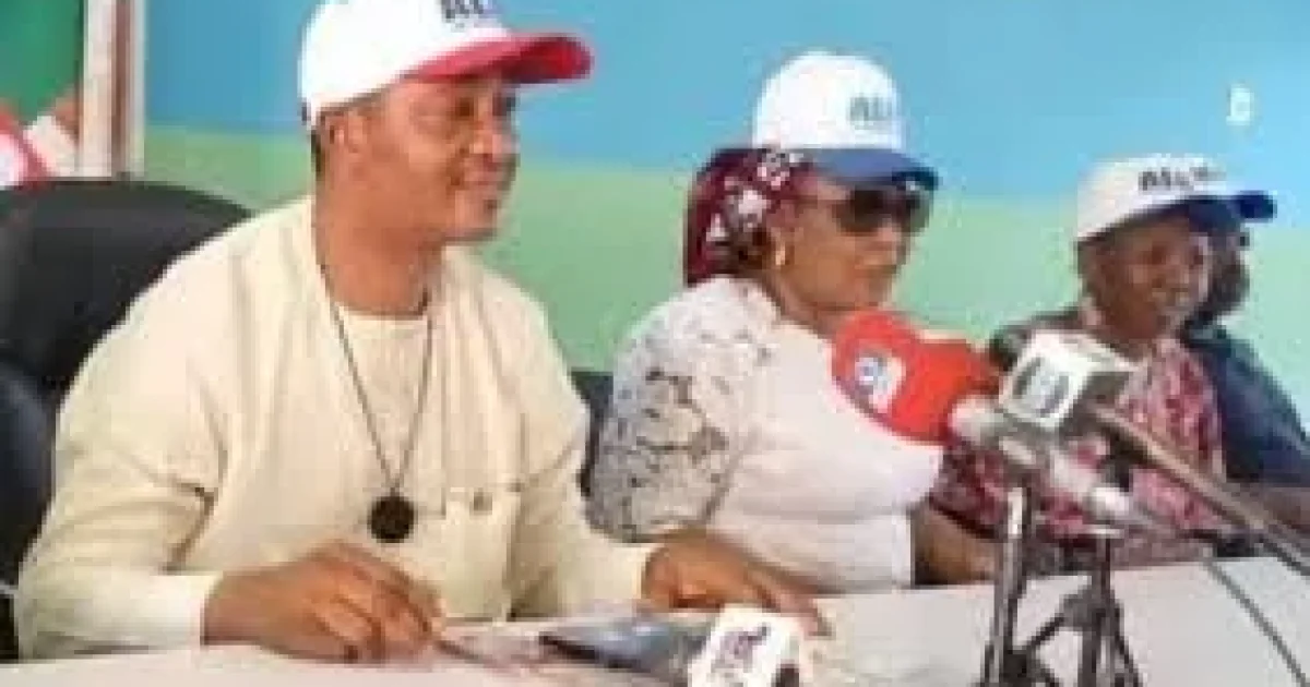 APC leaders seated at a press briefing table wearing party caps and addressing journalists