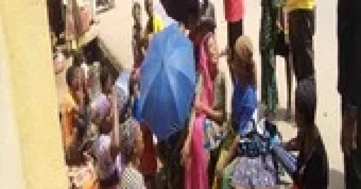 Beggars, including elderly men, women and children, seated along a busy Abuja street with bowls extended as pedestrians and vehicles pass by.